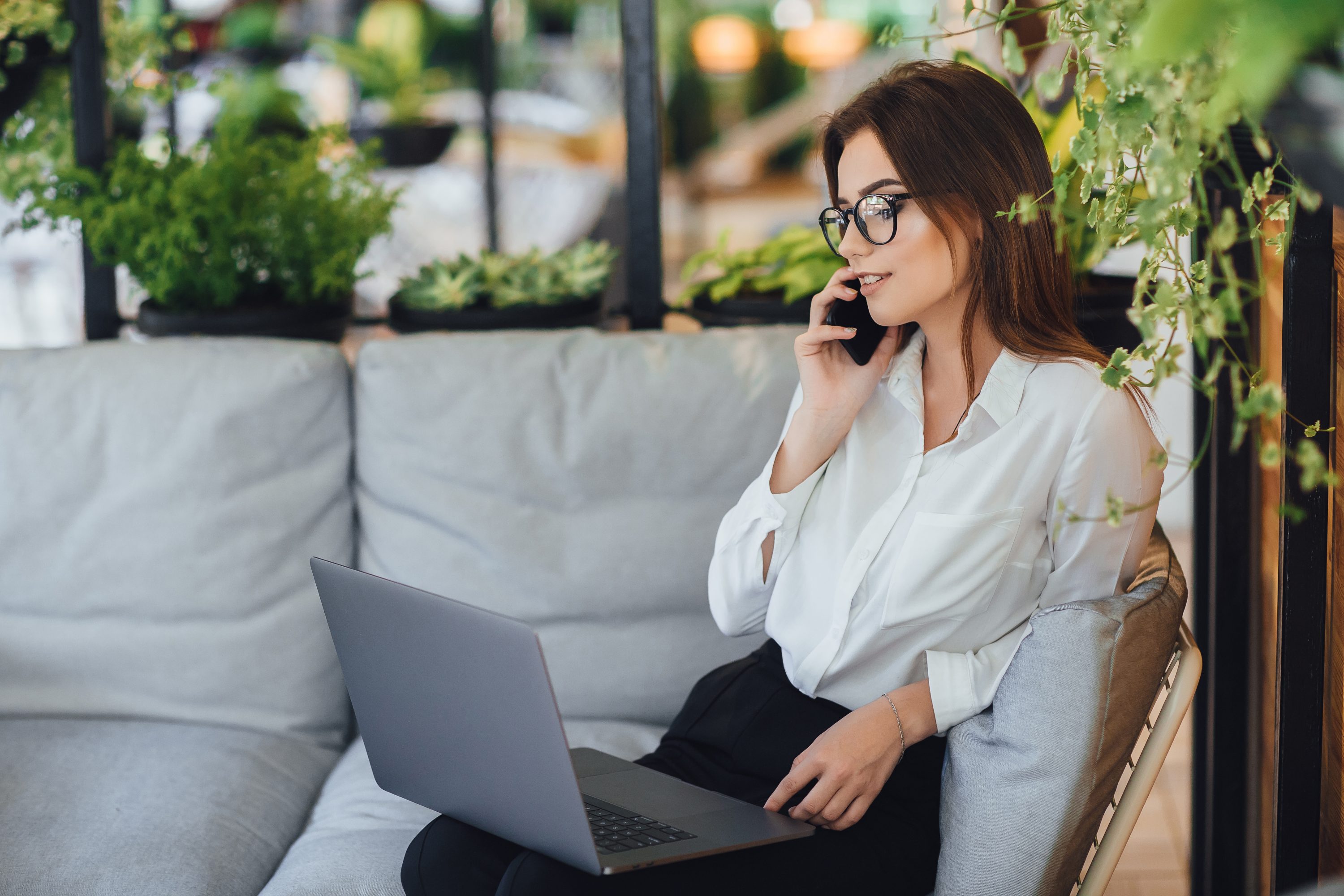 young beautiful woman works on laptop on the summer terrace of her modern office and talks over the phone scaled